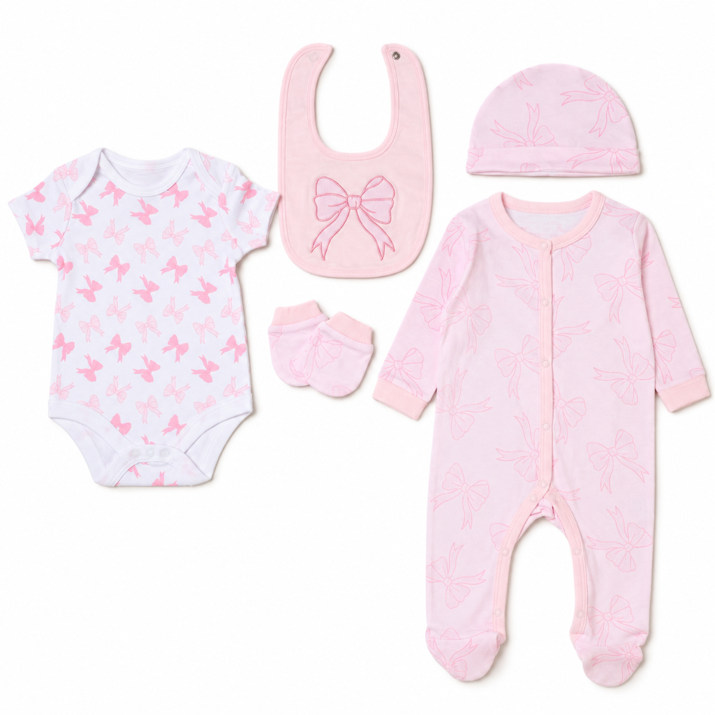 A 5-piece baby clothing set laid out on a white background, including a short-sleeve bodysuit, a footed one-piece, a bib, a beanie, and booties. The bodysuit and one-piece feature a light pink bow pattern on a white base, while the bib, beanie, and booties are solid light pink.