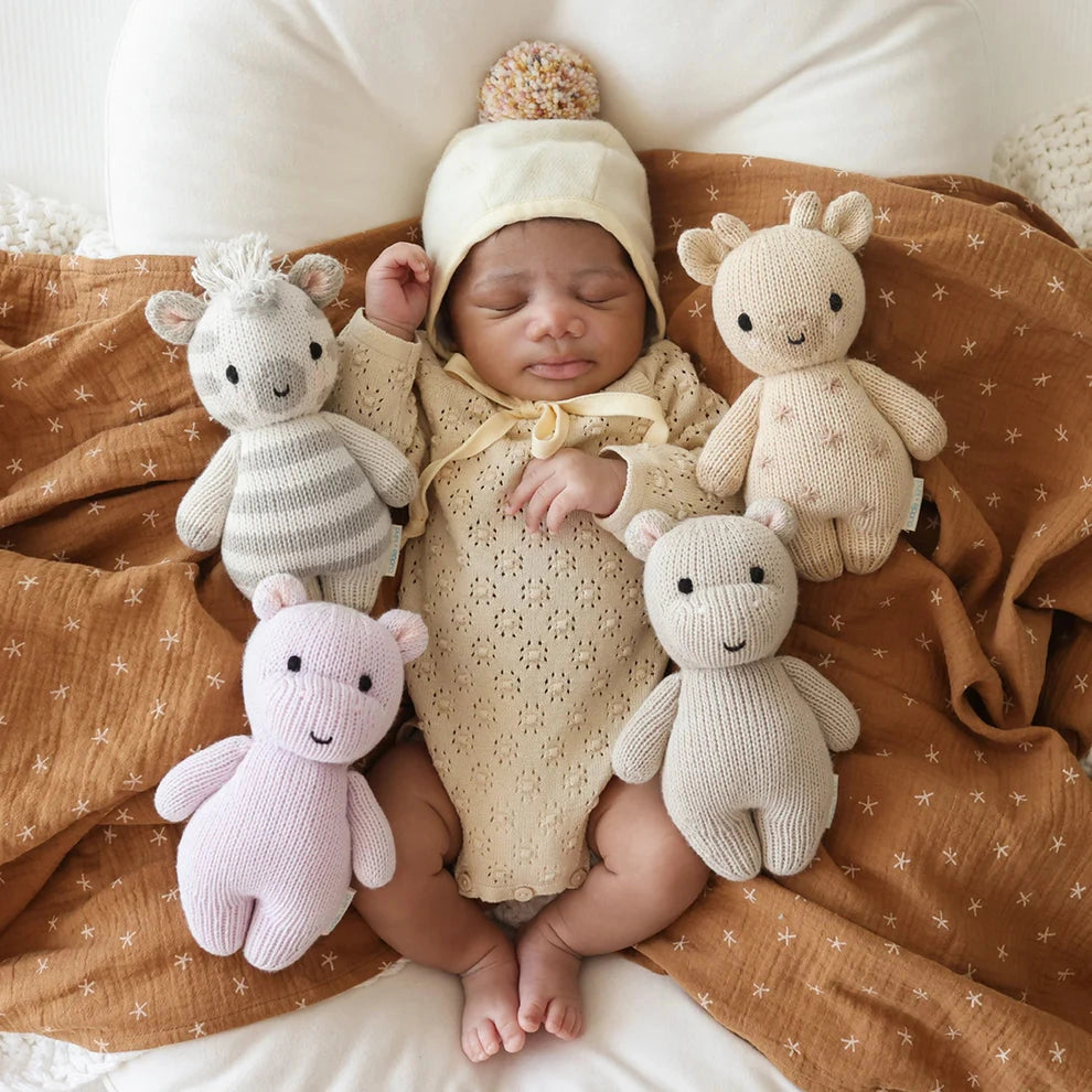 Newborn baby surrounded by knitted toys on a brown blanket