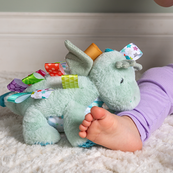 pale green dragon soft toy with brightly coloured taggies 