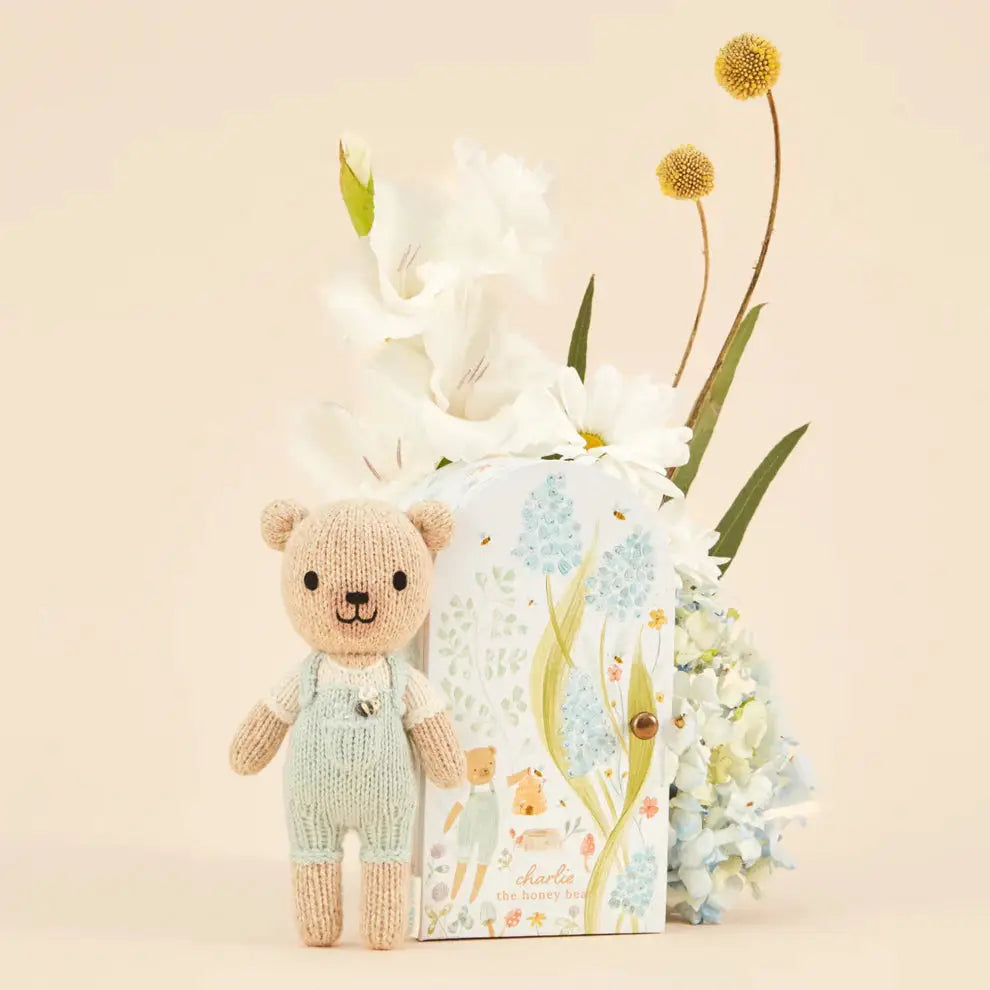 tiny charlie hand knitted bear in pale blue dungaree's with a honey bee