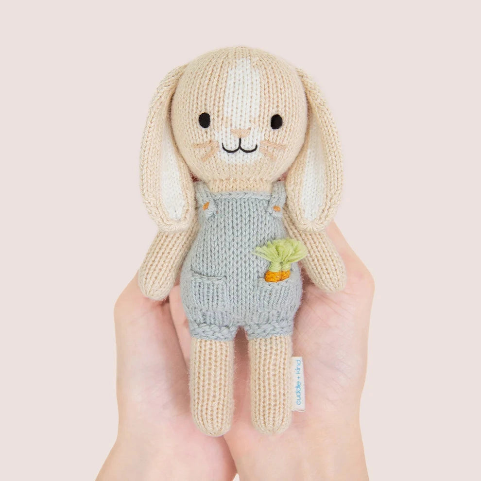 Knitted toy rabbit with a carrot in his pocket and light blue dungarees