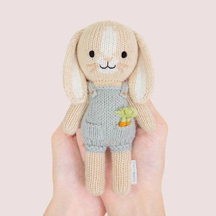 Knitted toy rabbit with a carrot in his pocket and light blue dungarees