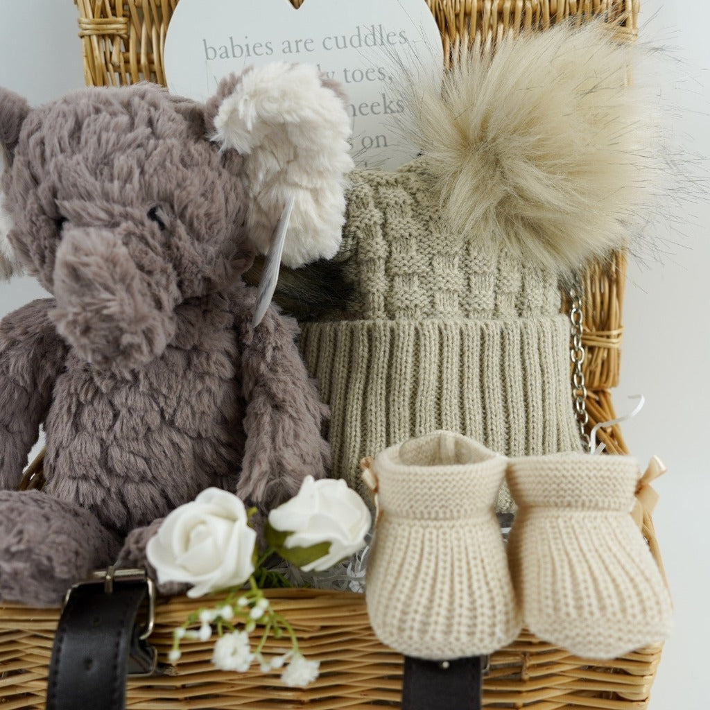 wicker hamper basket with grey elephant soft toy, nursery plaque, biscuit coloured knit booties, biscuit coloured double fluffy pom pom hat