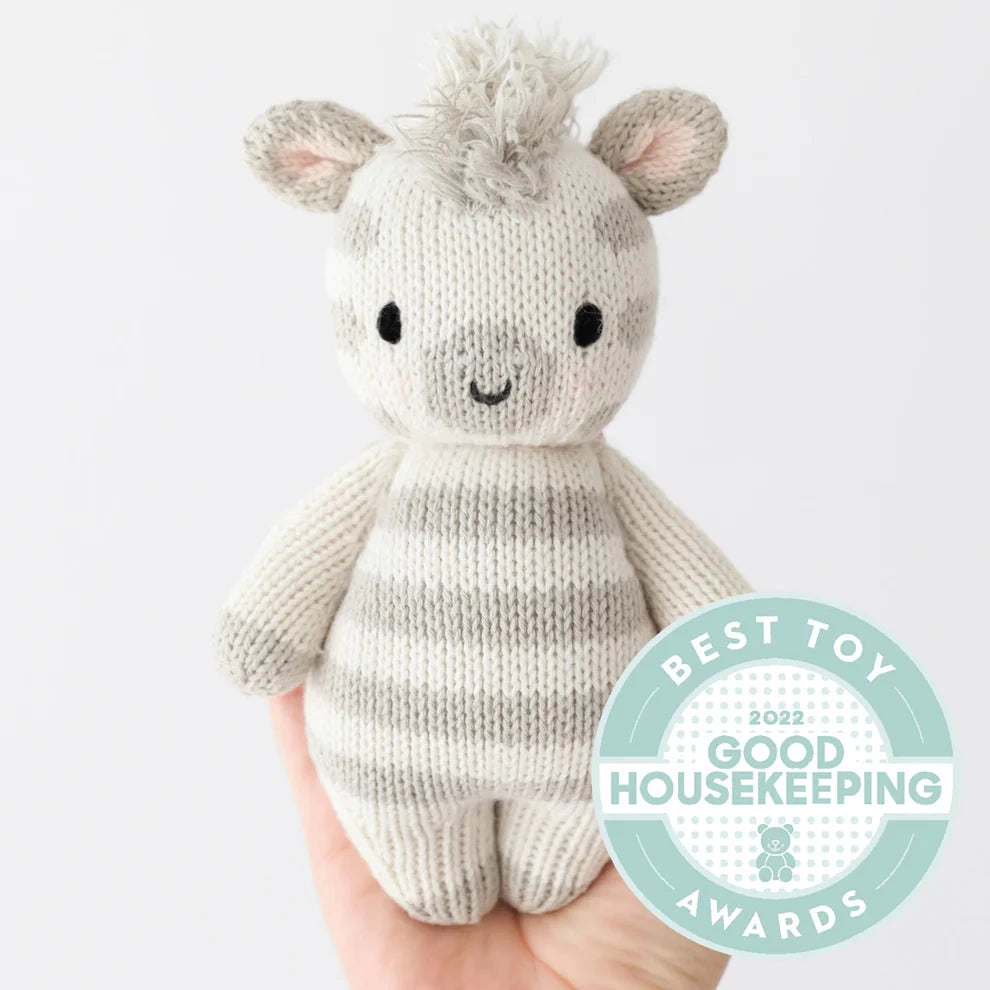 Knitted toy zebra held by a hand with Good Housekeeping Award badge on a white background