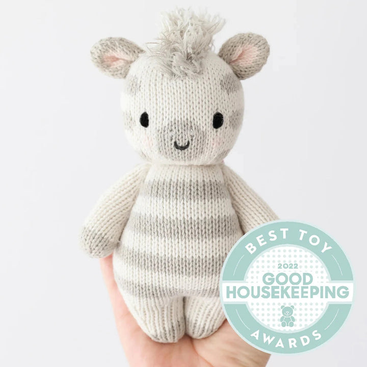 Knitted toy zebra held by a hand with Good Housekeeping Award badge on a white background