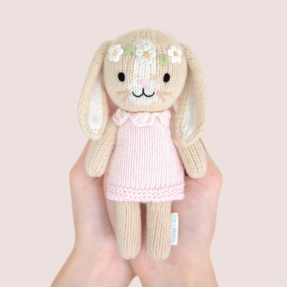 Handmade knitted bunny toy with a pink dress held in a hand against a plain background