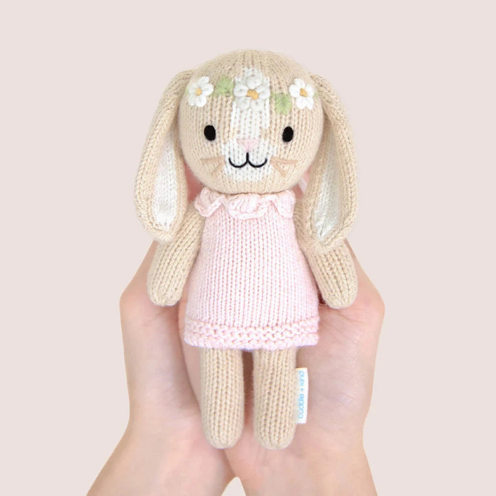 Handmade knitted bunny toy with a pink dress held in a hand against a plain background