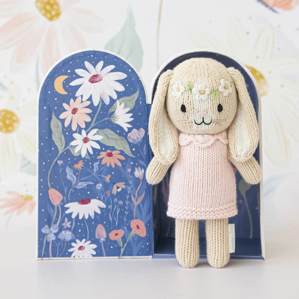 Knitted bunny toy in a pink dress with a floral background