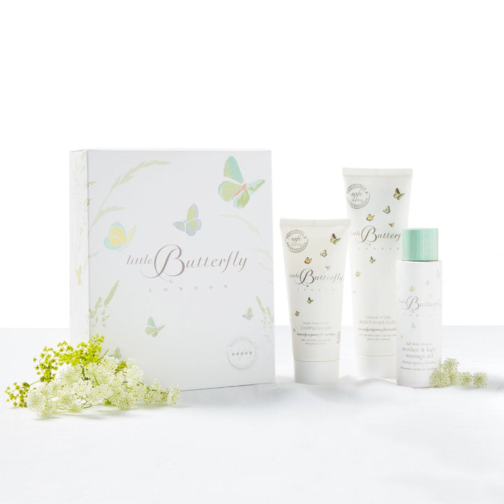 A pregnancy skincare gift set from Little Butterfly London featuring a white 'little Butterfly' box and three matching white tubes and bottles with delicate butterfly illustrations, green accents, and small white flowers placed around them 