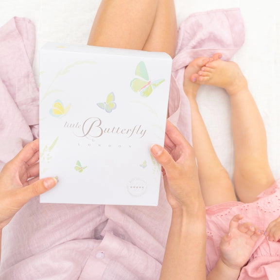 A pregnancy skincare gift set from Little Butterfly London featuring a white 'little Butterfly' box and three matching white tubes and bottles with delicate butterfly illustrations, green accents, and small white flowers placed around them