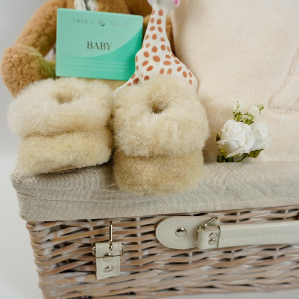 Luxury wicker baby and new mum hamper, cream velour baby sleepsuit with gold angel wings on the back, luxury ladies cream dressing gown with angel wings on the back, sophie la girafe teething toy, luxury alpaca baby slippers, luxury mother and baby candle, Steiff honey coloured teddy ben