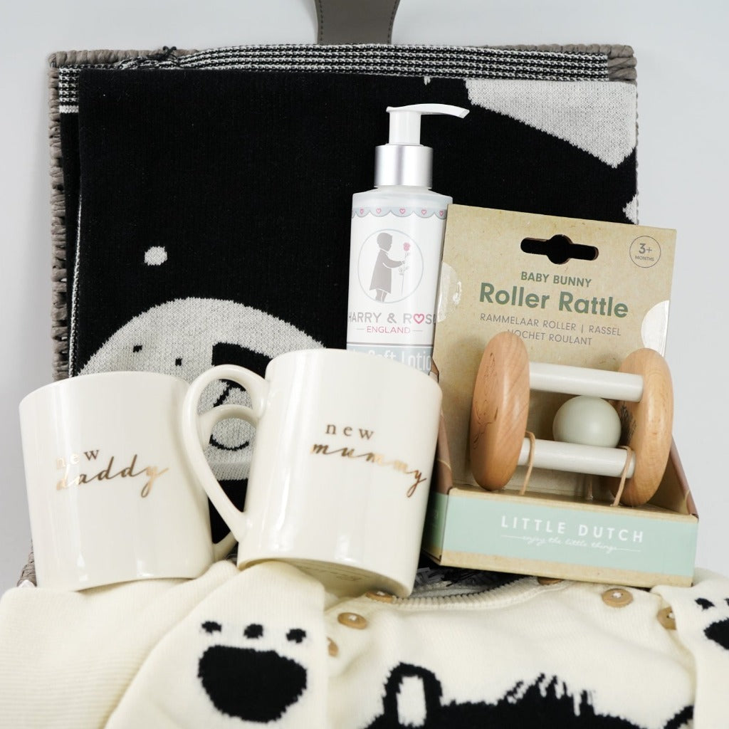 Neutral baby gift hamper, baby jumper in cream with black teddy face and matching cream joggers, New mummy and New daddy cream mugs with gold writing, wooden baby rattle, Black and cream teddy face baby blanket, organic baby lotion