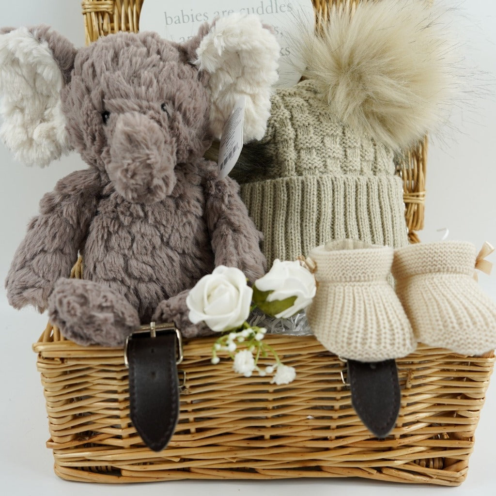 wicker hamper basket with grey elephant soft toy, nursery plaque, biscuit coloured knit booties, biscuit coloured double fluffy pom pom hat