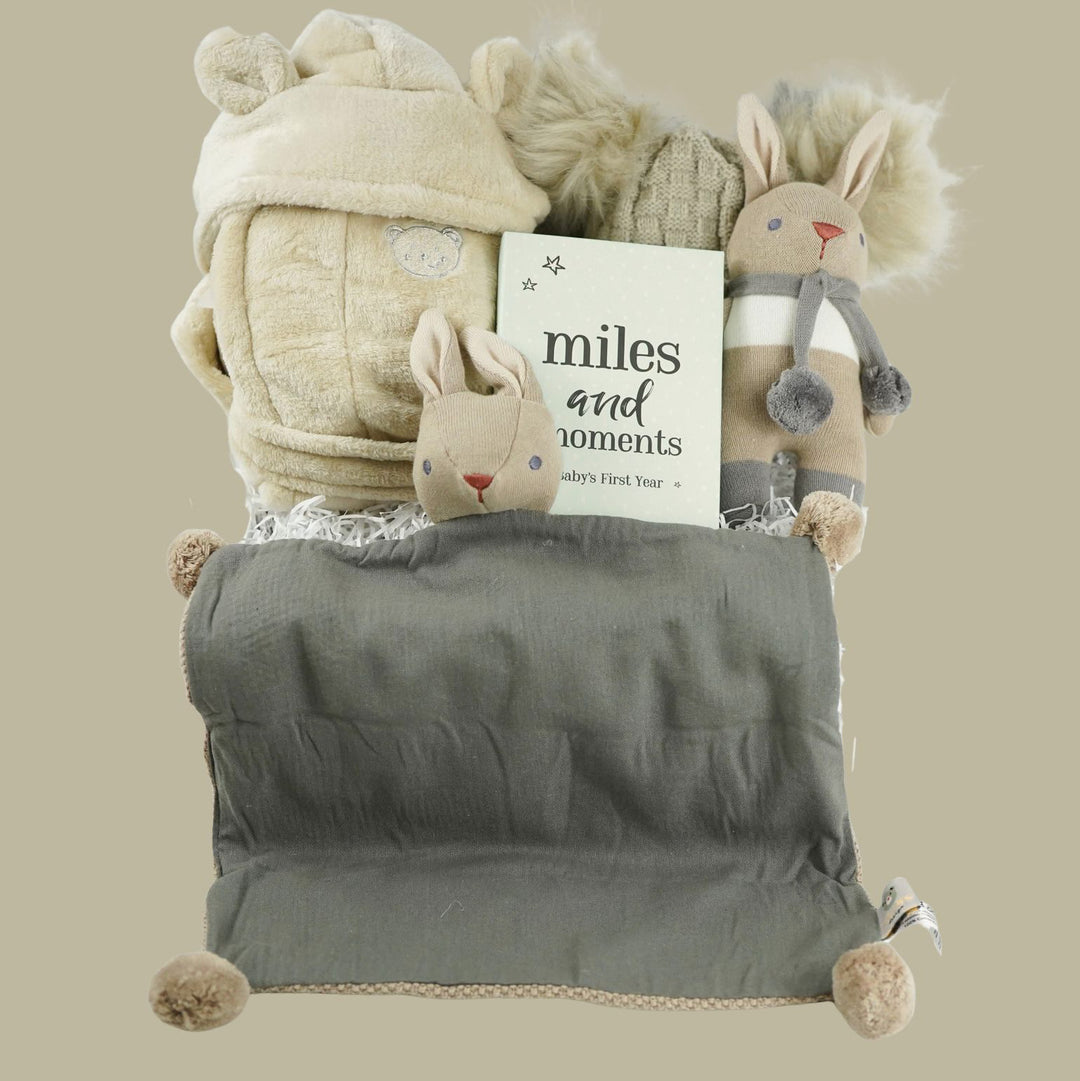 Collection of baby gift items including a comfort blanket, hat, and soft toy, baby dressing gown in neutral tones 