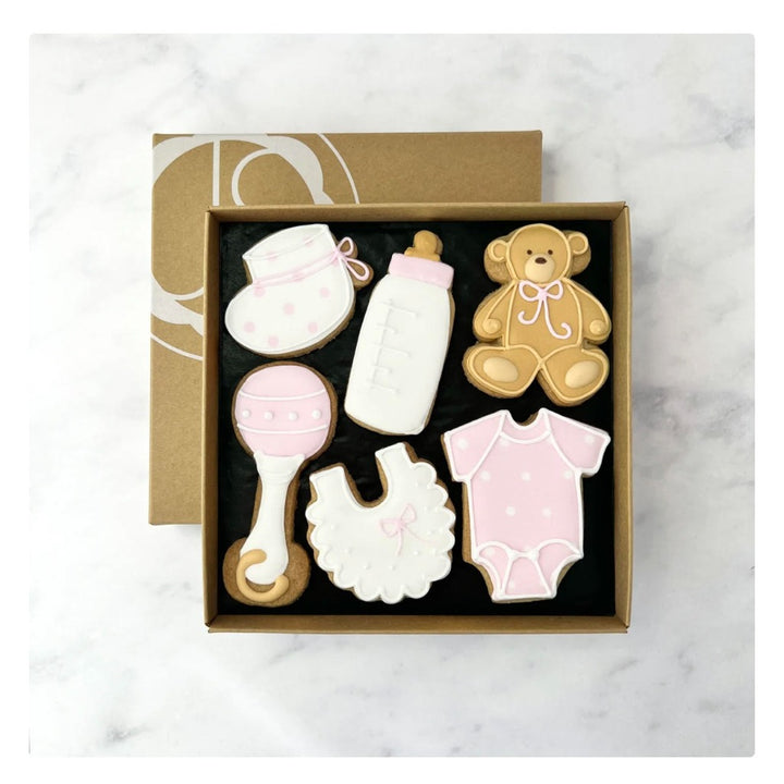 baby girl celebration biscuits in the shape of baby booties, rattle, bib, sleepsuit, teddy and baby bottle