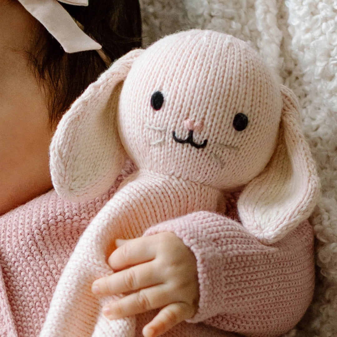 Knitted pink bunny held by a child with a soft focus background