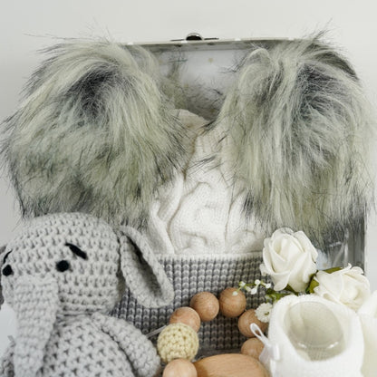 Grey gift suitcase with white stars, cream baby hat with grey trim and grey fluffy double pom poms , grey amigurumi elephant and wooden elephant teether with wooden and crocheted beads , white baby booties
