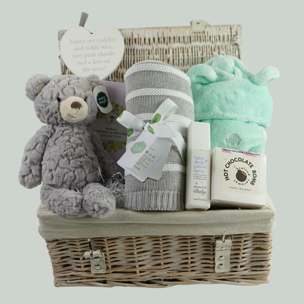 white wicker hamper basket, Neals ayard Organic Mum toiletries, Grey soft baby teddy, mint green baby dressing gown with cute ears, hot chocolate bomb, baby sleep pillow spray, grey and white stripe ziggle baby blanket