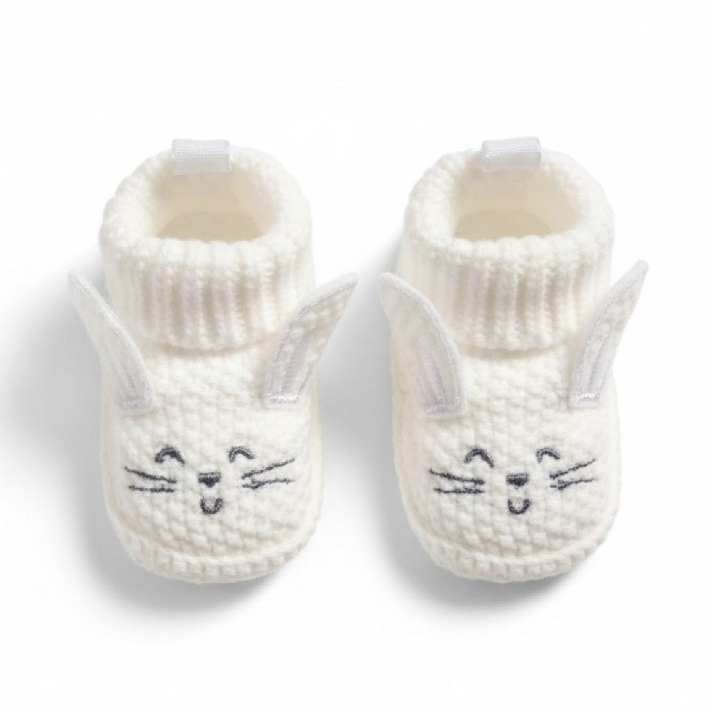 Pair of white knit baby booties with cat face design on a white background