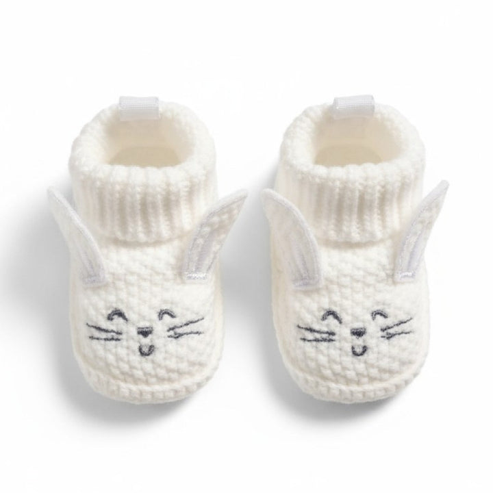 Pair of white knit baby booties with cat face design on a white background