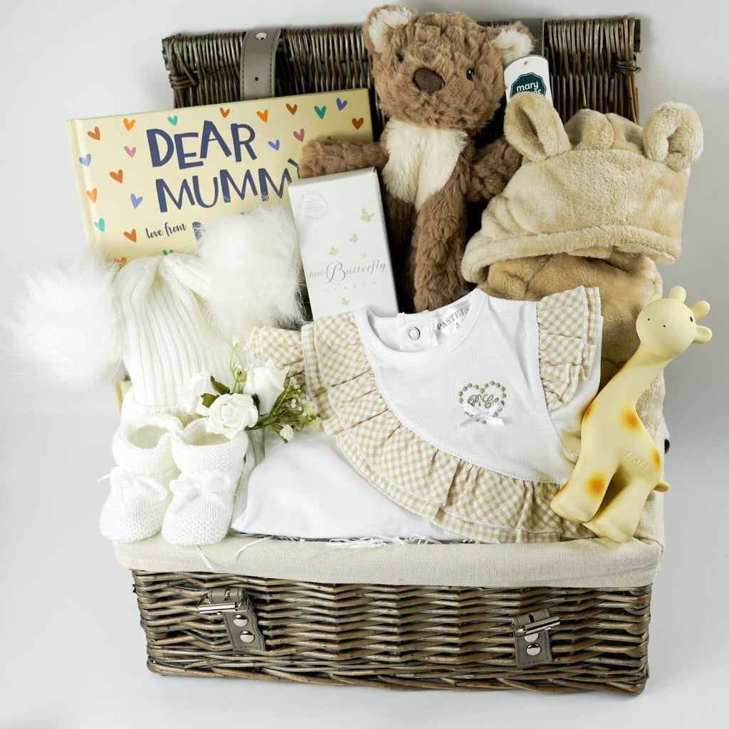 Natural hamer basket with baby gifts includes luxury baby clothing in white with caramel check ruffles, baby book, soft teddy comforter, baby dressing gown with ears, fluffy hat with double pom poms in white, natural baby toiletries, knitted booties , baby natural rubber bath toy/teether in Girafee shape