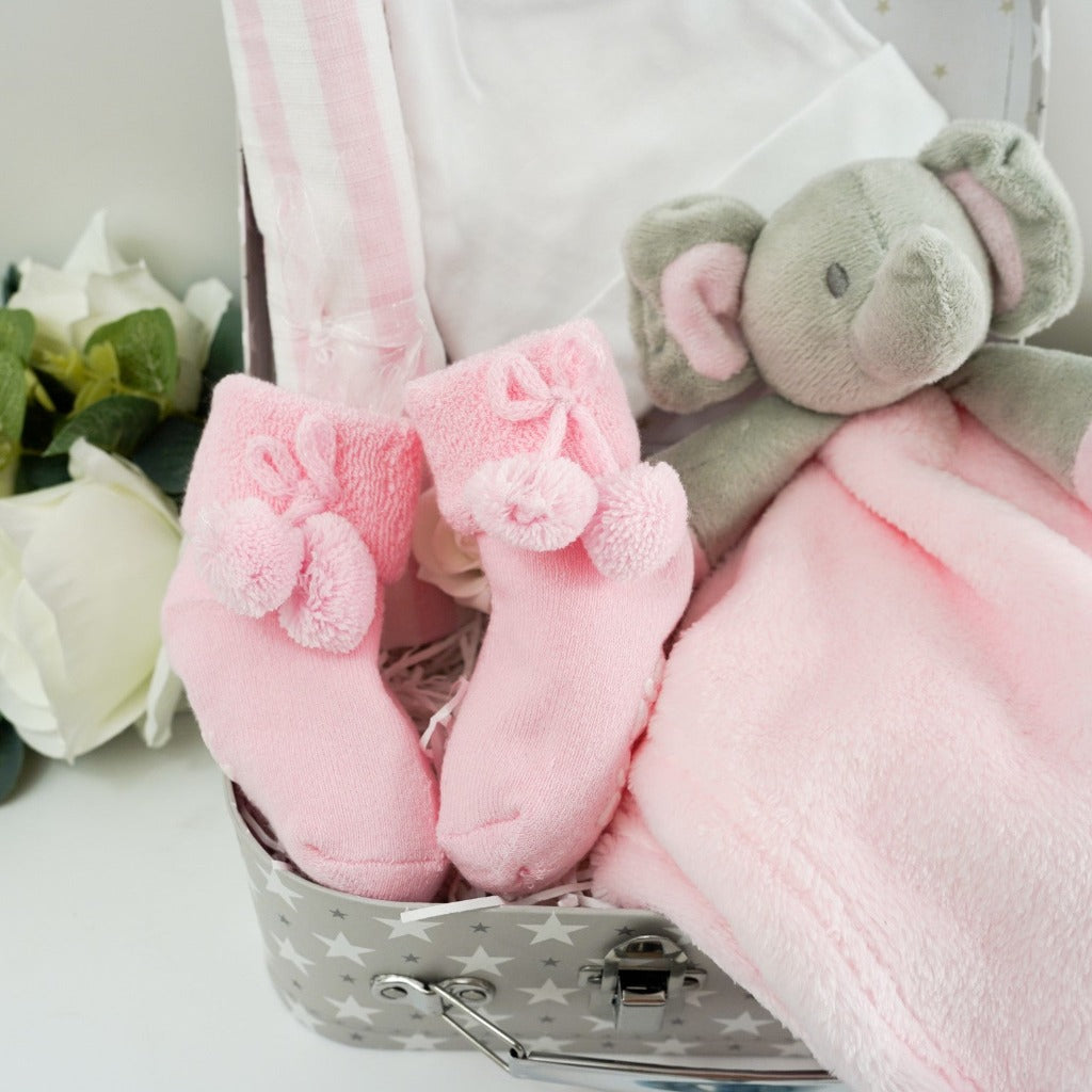 Small gift case with baby pink socks with cute writing on the sole, pink muslin, white baby knot hat, pink elephant baby comforter