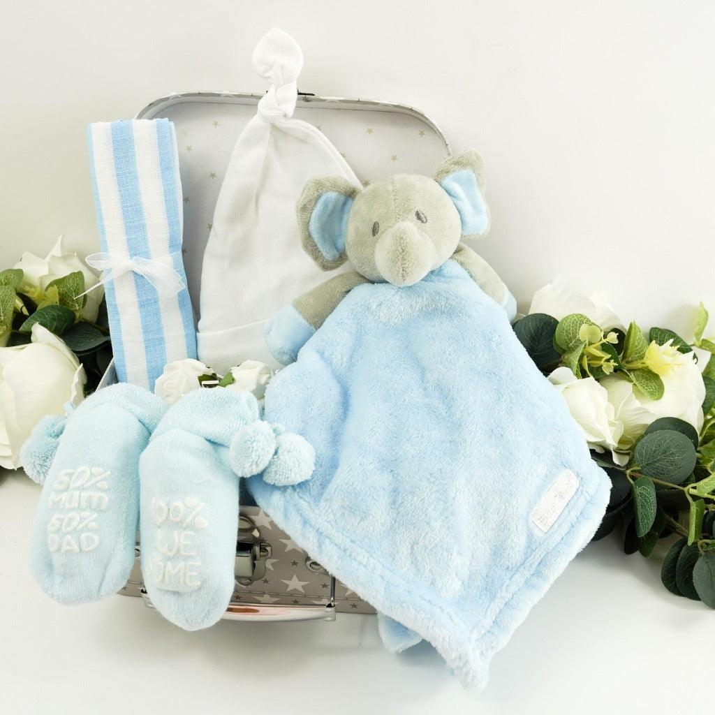 small baby hamper in a grey and white gift case, blue muslin, blue socks with pom poms and cute writing on the sole, baby knot hat in white , soft blue and grey baby elephant comforter