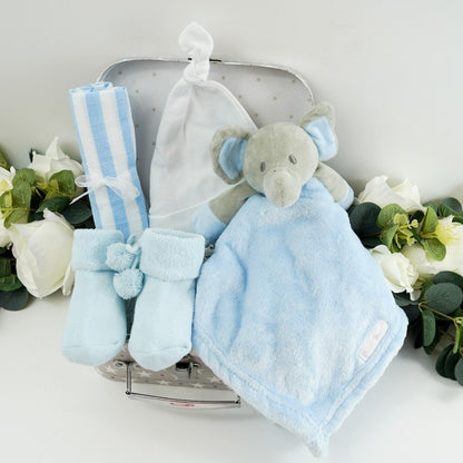 small baby hamper in a grey and white gift case, blue muslin, blue socks with pom poms and cute writing on the sole, baby knot hat in white , soft blue and grey baby elephant comforter 