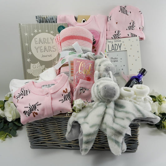 Natural baby hamper basket with pink baby set including pink baby sleepsuit with zebra's, white baby zest, pink baby hat with zebra's, pink baby mittens with zebra's, baby hat with zebra's, baby early years journal,  baby picture frame with pink elephant, luxury ziggle blanket pink with stripes,  luxury chocolate bar, neals yard mothers bath oil, eco friendly zebra  soft baby toy in white and grey stripe,  zebra comforter in white with grey stipes