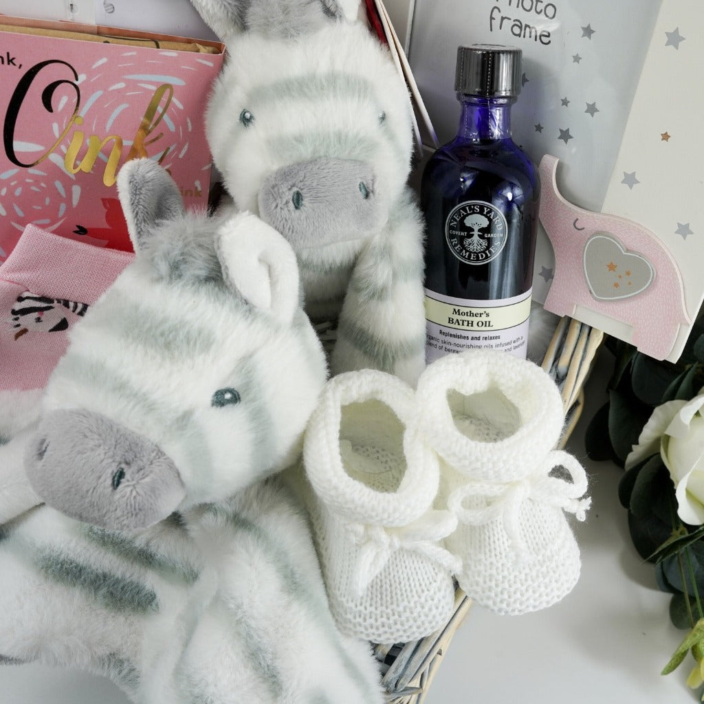Natural baby hamper basket with pink baby set including pink baby sleepsuit with zebra's, white baby zest, pink baby hat with zebra's, pink baby mittens with zebra's, baby hat with zebra's, baby early years journal, baby picture frame with pink elephant, luxury ziggle blanket pink with stripes, luxury chocolate bar, neals yard mothers bath oil, eco friendly zebra soft baby toy in white and grey stripe, zebra comforter in white with grey stipes