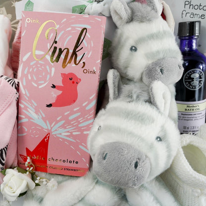Natural baby hamper basket with pink baby set including pink baby sleepsuit with zebra's, white baby zest, pink baby hat with zebra's, pink baby mittens with zebra's, baby hat with zebra's, baby early years journal, baby picture frame with pink elephant, luxury ziggle blanket pink with stripes, luxury chocolate bar, neals yard mothers bath oil, eco friendly zebra soft baby toy in white and grey stripe, zebra comforter in white with grey stipes