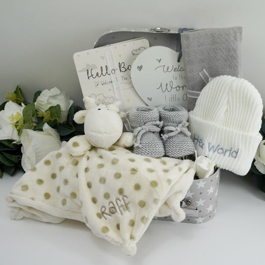 Cream spot giraffe  comforter in a neutral colour with a rattle inside, white baby beanie ribbed hat with welcome to the world written on, grey knitted booties with a tie, memorable moments cards , white plaque for the nursery with silver writing welcome to the world , soft grey muslin