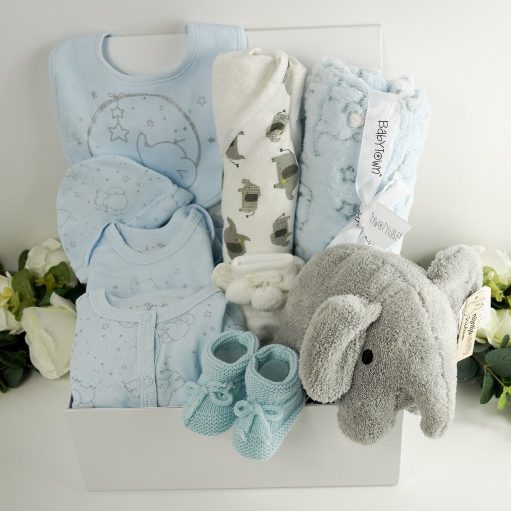 Elephant themed baby gift including a blue 100% cotton baby set with grey elephants, white hooded baby towel with grey elephants, soft pale blue baby blanket with elephants and stars , white baby pom pom socks, soft blue kitted baby bootied , grey terry miffy elephant soft baby toy all in a white hamper box