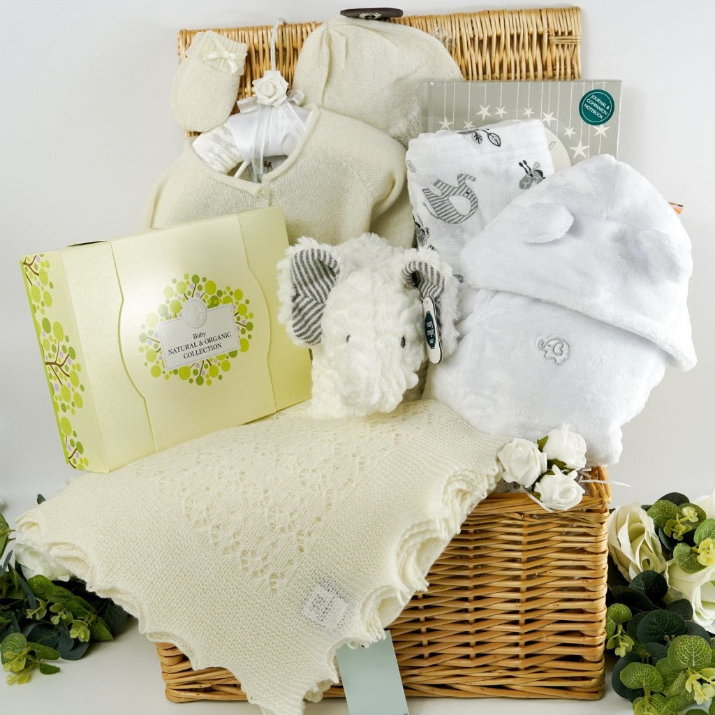 Baby hamper basket in natural willow, cashmere baby cardigan in soft white , cashmere baby hat and mittens in soft white, cashmere  heirloom shawl in soft white, baby neals yard organic toiletries, baby white dressing gown with cute ears , soft muslin swaddle, cute white soft musical elephant toy , baby journal from birth to five years in grey and white 