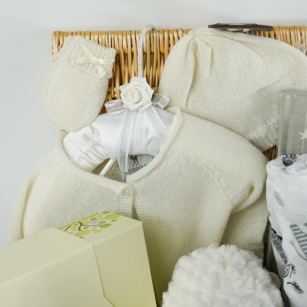 Baby hamper basket in natural willow, cashmere baby cardigan in soft white , cashmere baby hat and mittens in soft white, cashmere heirloom shawl in soft white, baby neals yard organic toiletries, baby white dressing gown with cute ears , soft muslin swaddle, cute white soft musical elephant toy , baby journal from birth to five years in grey and white