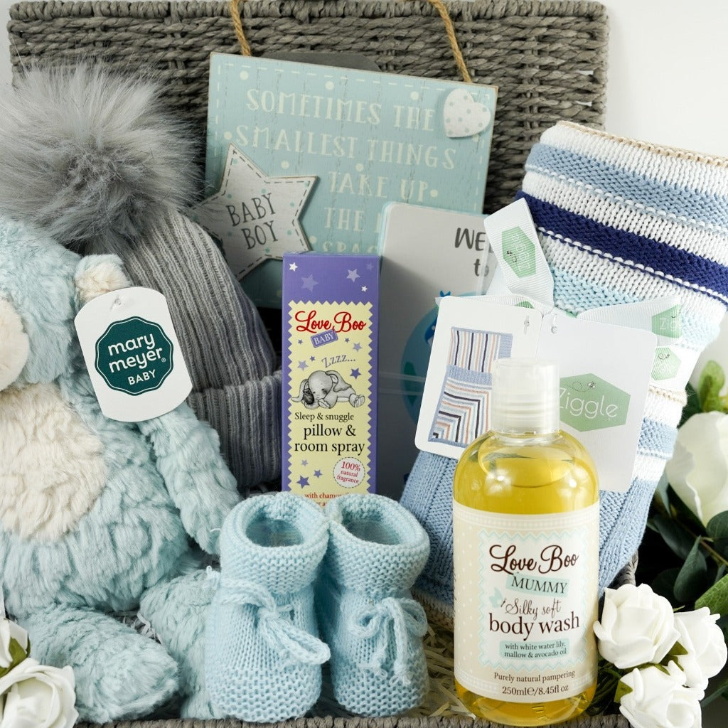 Grey baby hamper basket with soft blue and white monkey by Mary Meyer, grey pom pom baby hat, baby blue knit booties, baby boy room plaque with writing, Ziggle blue stipe heavy knit blanket, Love Boo pillow spray , Love boo mummy body wash