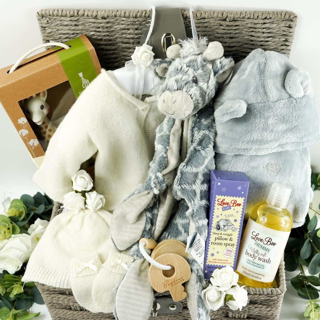 Grey hamper basket with baby gift items including soft white baby cashmere cardigan, soft white baby cashmere baby hat, soft cashmere baby mittens with a bow, sophie la giraffe baby toy and teething toy, grey soft fleece baby dressing gown with ears, grey soft elephant blanket comforter with knot ends, baby pillow and room spray by Love boo, mum silky wash by Love boo, wooden key shaped teether