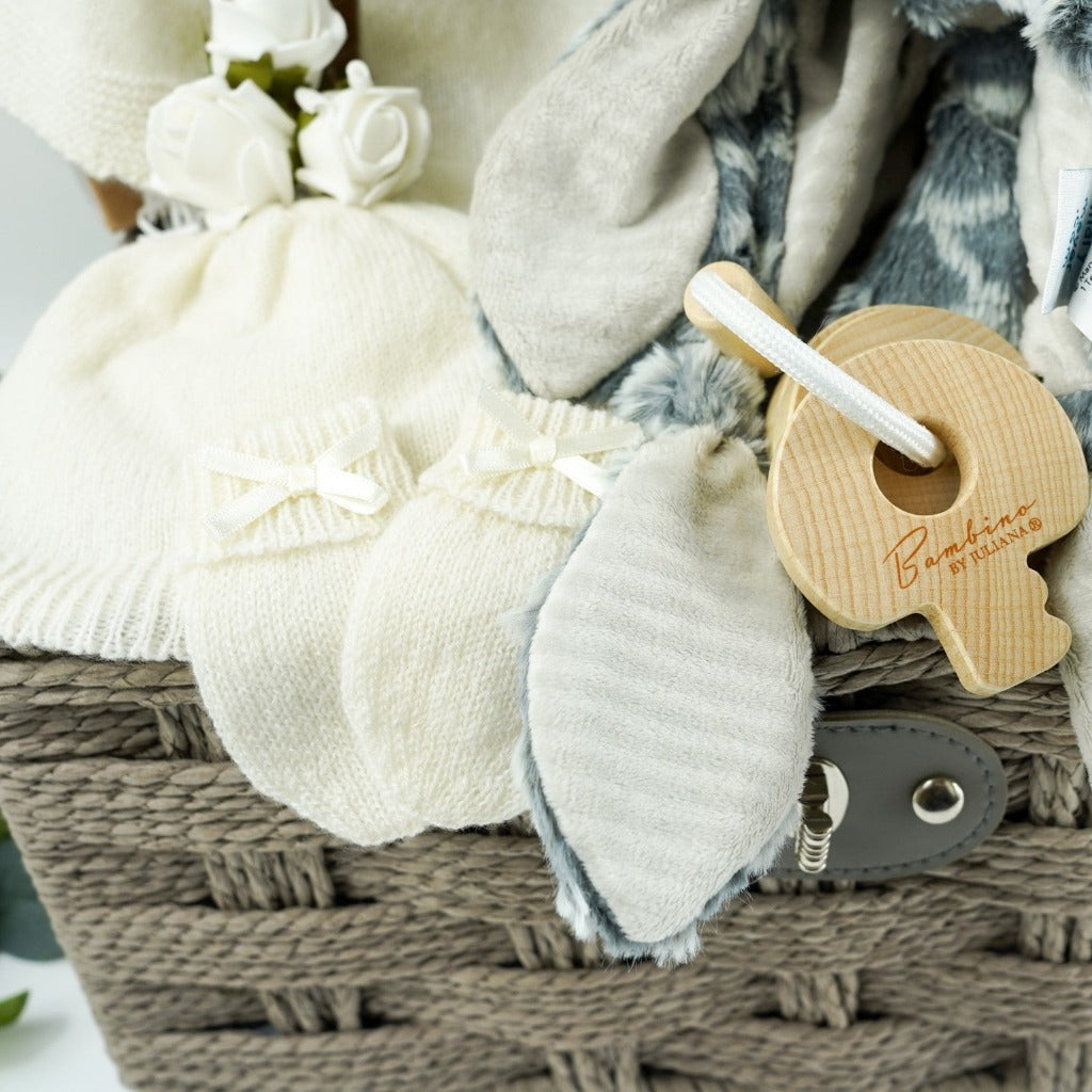 Grey hamper basket with baby gift items including soft white baby cashmere cardigan, soft white baby cashmere baby hat, soft cashmere baby mittens with a bow, sophie la giraffe baby toy and teething toy, grey soft fleece baby dressing gown with ears, grey soft elephant blanket comforter with knot ends, baby pillow and room spray by Love boo, mum silky wash by Love boo, wooden key shaped teether