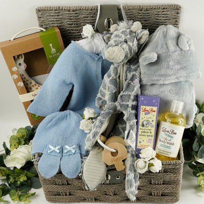 Grey hamper basket with baby gift items including soft blue baby cashmere cardigan, soft white baby cashmere baby hat, soft cashmere baby mittens with a bow, sophie la giraffe baby toy and teething toy, grey soft fleece baby dressing gown with ears, grey soft elephant blanket comforter with knot ends, baby pillow and room spray by Love boo, mum silky wash by Love boo, wooden key shaped teether