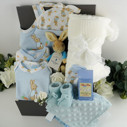 Grey magnetic baby hamper, baby boy Peter Rabbiot clothing set, blue body suit with peter rabbit embroidered design,  white baby sleepsuit with rabbits, peter rabbit design baby hat with knot, baby mittens, blue bib with Pter Rabbit embroidered, white knit pom pom blanket, blue bubble comforter with ribbon tabs, baby massage oil by Love boo, Peter rabbit rattle soft toy
