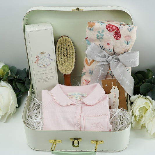 Pale green baby gift suitcase by Marie- Chantal, pink prmium cottom baby sleepsuit with angel wings embroidered  on the pocket and picot edging, natural wooden baby hair  brush, baby swaddle muslin in pink with butterly design tied with a ribbon