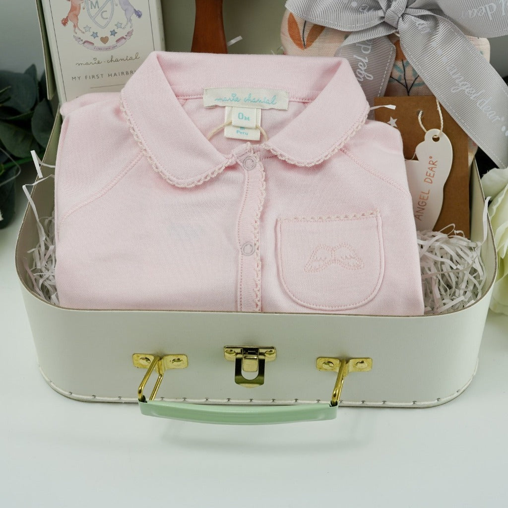 Pale green baby gift suitcase by Marie- Chantal, pink prmium cottom baby sleepsuit with angel wings embroidered on the pocket and picot edging, natural wooden baby hair brush, baby swaddle muslin in pink with butterfly design tied with a ribbon
