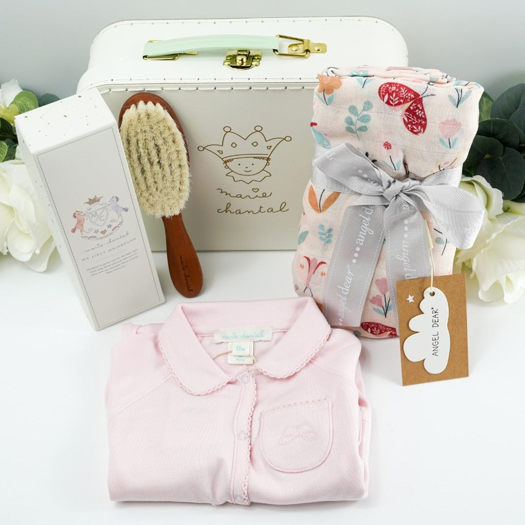 Pale green baby gift suitcase by Marie- Chantal, pink prmium cottom baby sleepsuit with angel wings embroidered on the pocket and picot edging, natural wooden baby hair brush, baby swaddle muslin in pink with butterfly design tied with a ribbon