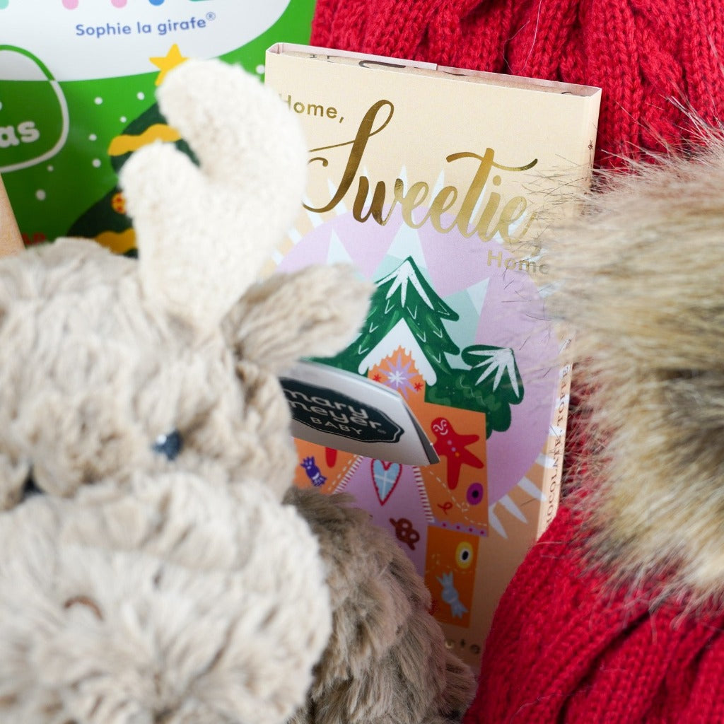White magnetic ribbon tabbed, with baby and new mum gifts , matching red bobble hats for mum and baby, Sofie La Giraffe soft teether giraffe, Sophie La Giraffe first christmas baby book, soft cuddly brown moose by Mary Meyer, soft white knit booties