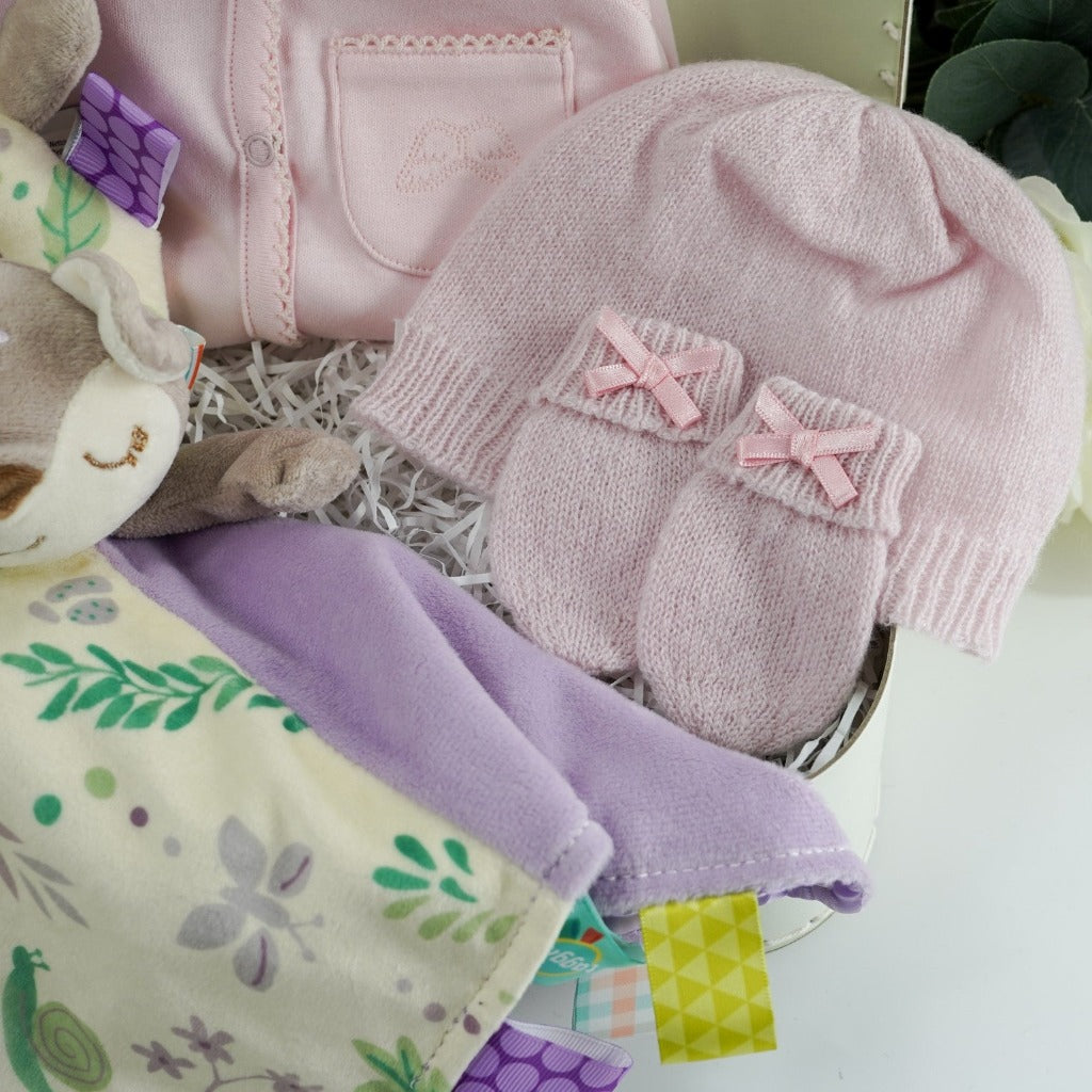 Marie Chantal baby gift suitcase in pale green with Marie Chantal logo, pink picot edge baby sleepsuit with angel wings embroidered on the pocket, pink cashmere baby hat and mittens by GH Hurt, soft floral fawn taggie blanket by Mary meyer and matching fawn floral rattle