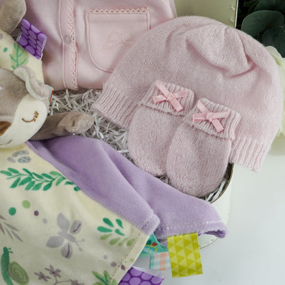Marie Chantal baby gift suitcase in pale green with Marie Chantal logo, pink picot edge baby sleepsuit with angel wings embroidered on the pocket, pink cashmere baby hat and mittens by GH Hurt, soft floral fawn taggie blanket by Mary meyer and matching fawn floral rattle