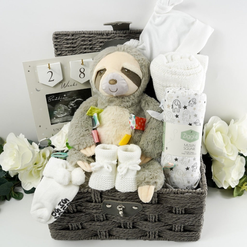 Grey hamper basket with mum to be gifts including a countdown picture fram for the first scan and hooks with numbers to countdown the weeks of pregnancy, mary meyer sloth with taggies, white muslin with grey and black elephants , softs with writing on the sole and pom pom, white knit booties with a tie, soft white cellular baby blanket, white cotton baby hat with 2 knotted corners 