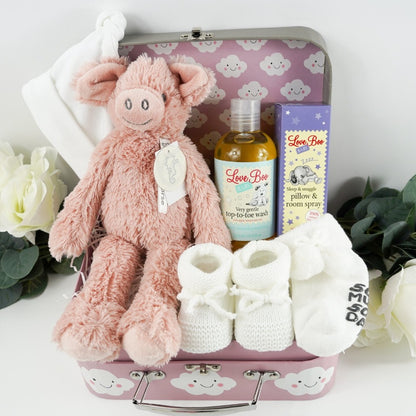 pink baby gift case with white clouds includes a soft pink pig by Happy Horse, soft white knit baby booties with a tie, soft white socks with writing on the sole, white cotton baby hat with two knotted corners, Love boo room and pillow spray, love boo baby wash