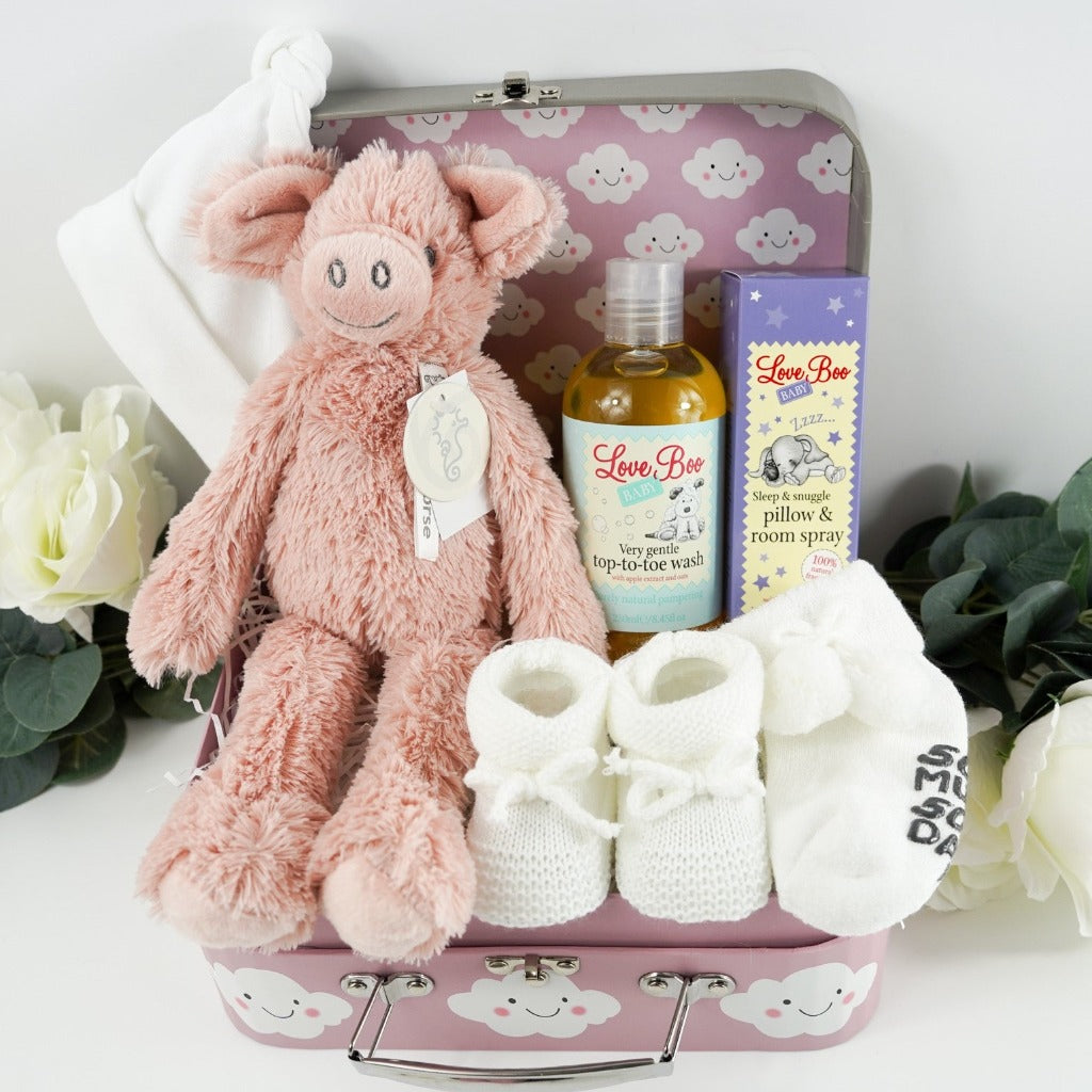 pink baby gift case with white clouds includes a soft pink pig by Happy Horse, soft white knit baby booties with a tie, soft white socks with writing on the sole, white cotton baby hat with two knotted corners, Love boo room and pillow spray, love boo baby wash