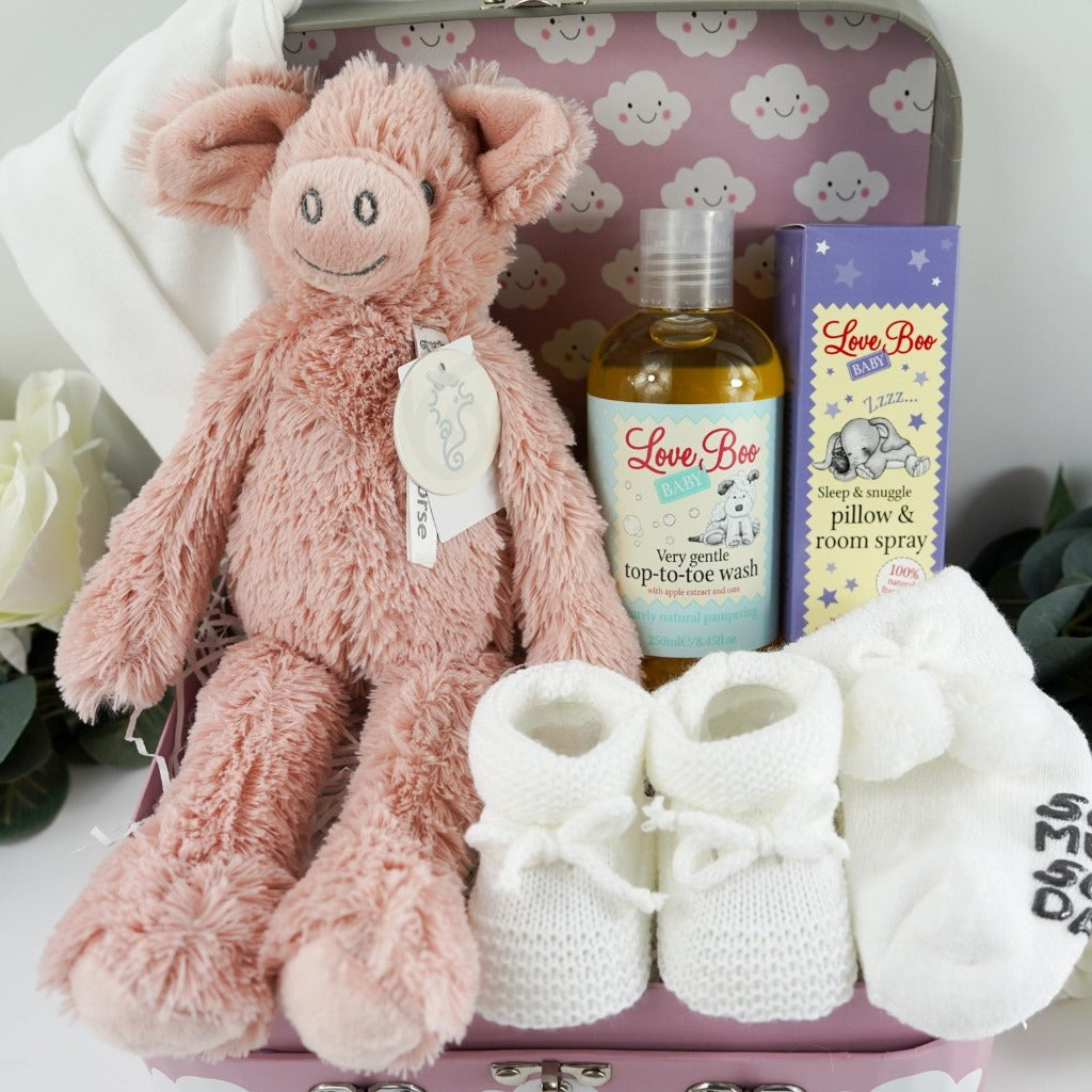 pink baby gift case with white clouds includes a soft pink pig by Happy Horse, soft white knit baby booties with a tie, soft white socks with writing on the sole, white cotton baby hat with two knotted corners, Love boo room and pillow spray, love boo baby wash